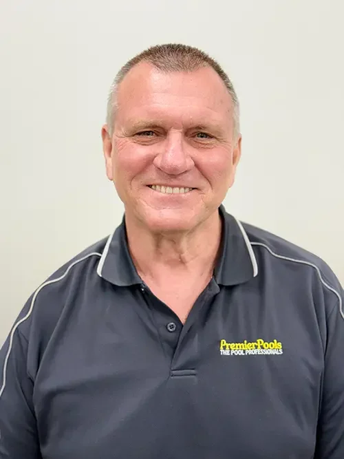A smiling man with short gray hair wearing a dark gray polo shirt with yellow text that reads 'PremierPools THE POOL PROFESSIONALS' standing against a plain light-colored background.