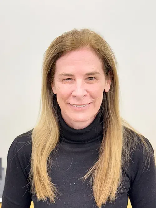 Image of a woman with long blonde hair wearing a black turtleneck sweater, smiling slightly in front of a plain light-colored background.