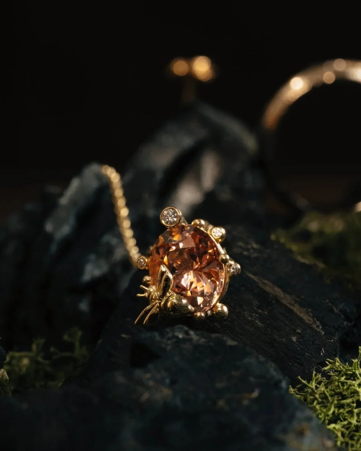 Gold jewelry with an orange gemstone and small diamonds on a dark, textured surface.