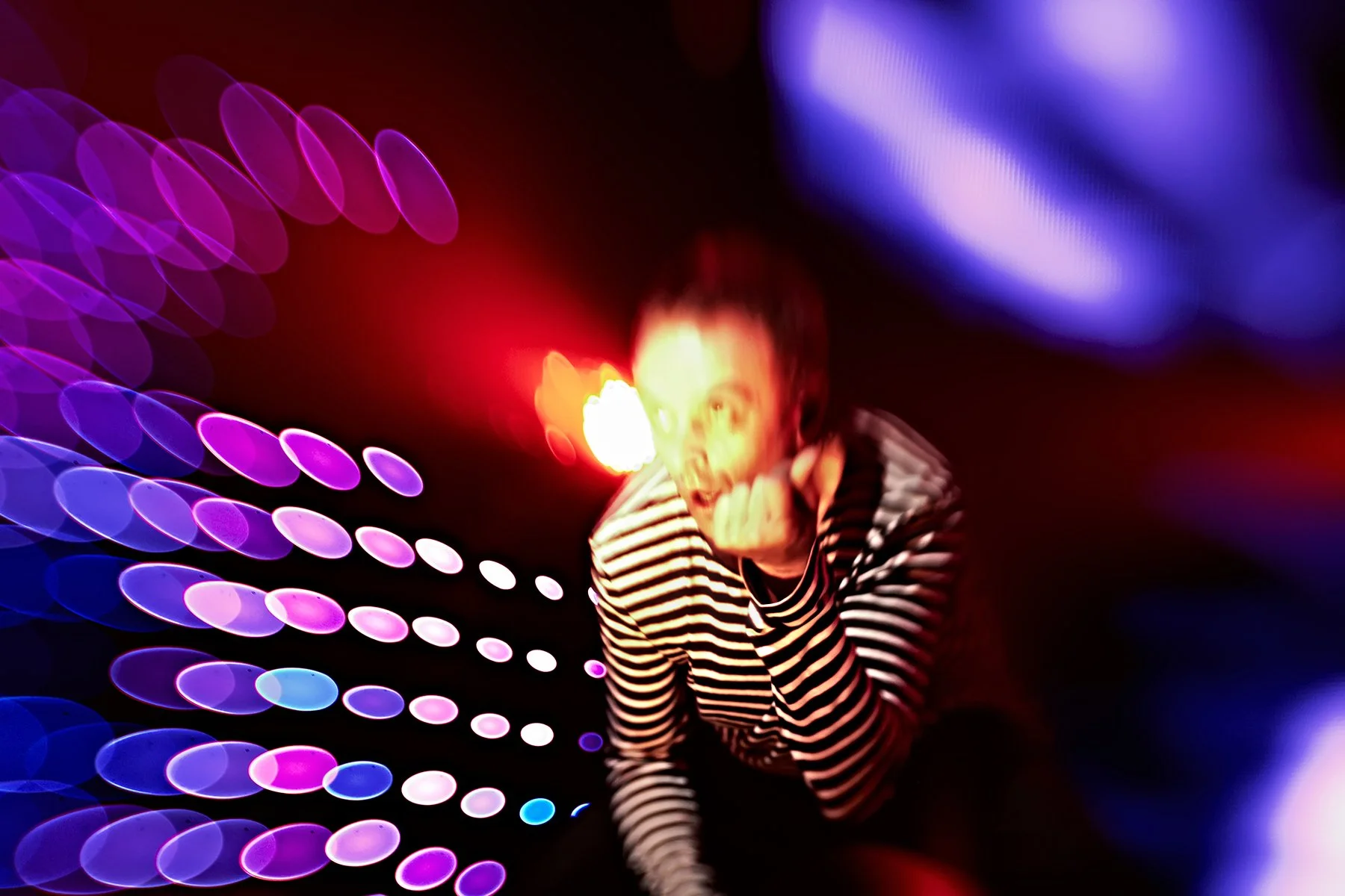 Blurred image of a person in a striped shirt with colorful abstract lights in the background.