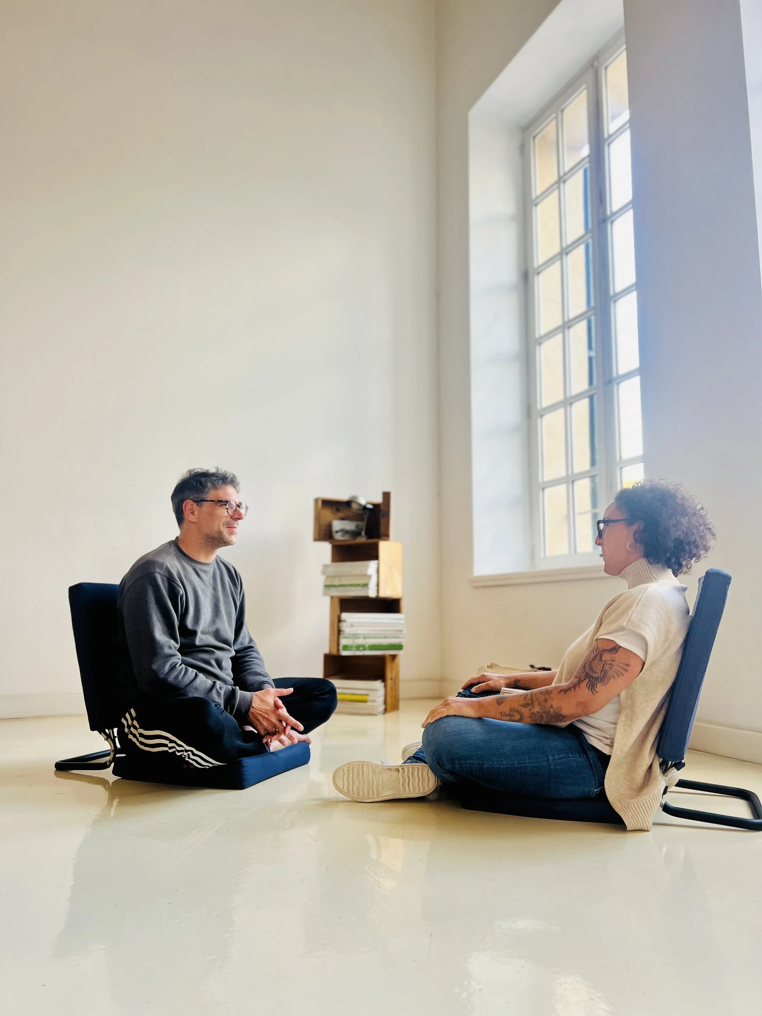 Two people sitting on cushions facing each other in a calm room with natural light, reflecting a somatic therapy session focused on presence and connection.