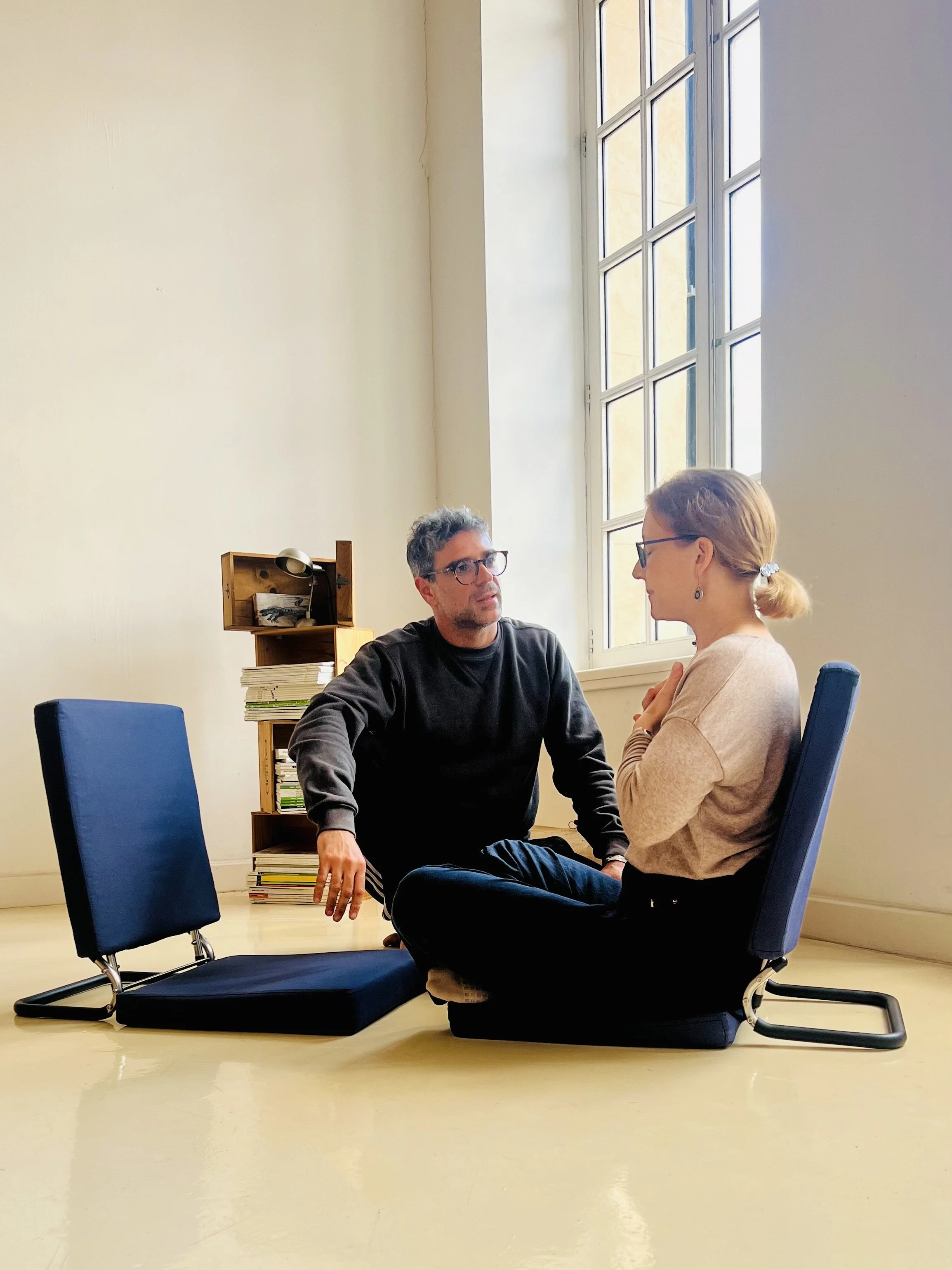 Two people seated on floor cushions in conversation during a Hakomi-inspired somatic therapy session in a quiet, light-filled space.