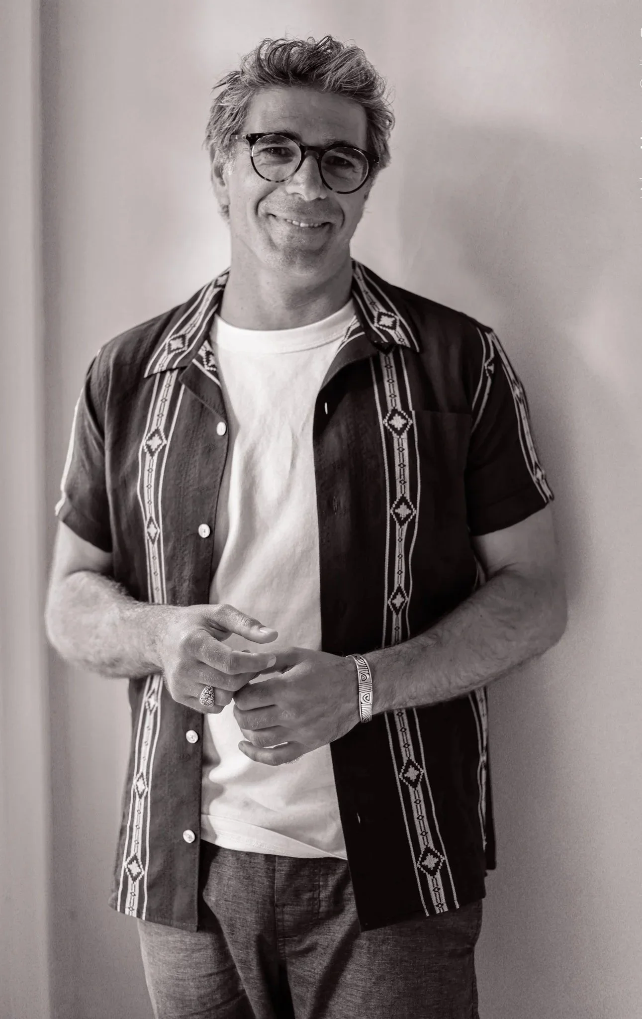 Black and white portrait of Odin, a psychedelic somatic therapist, smiling gently with hands clasped.