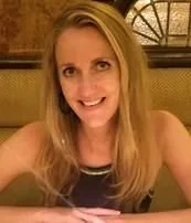 A woman with blonde hair smiling at the camera in a restaurant setting.