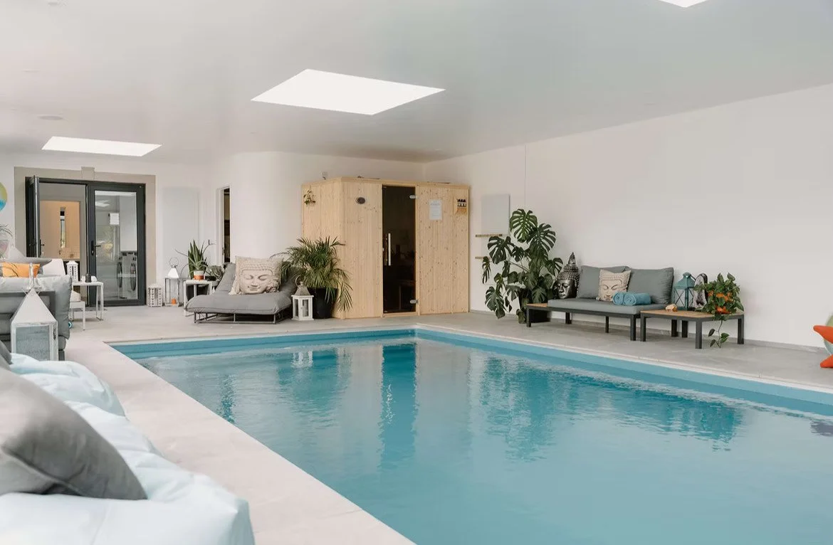 Indoor swimming pool area with lounge chairs, potted plants, and a sauna.