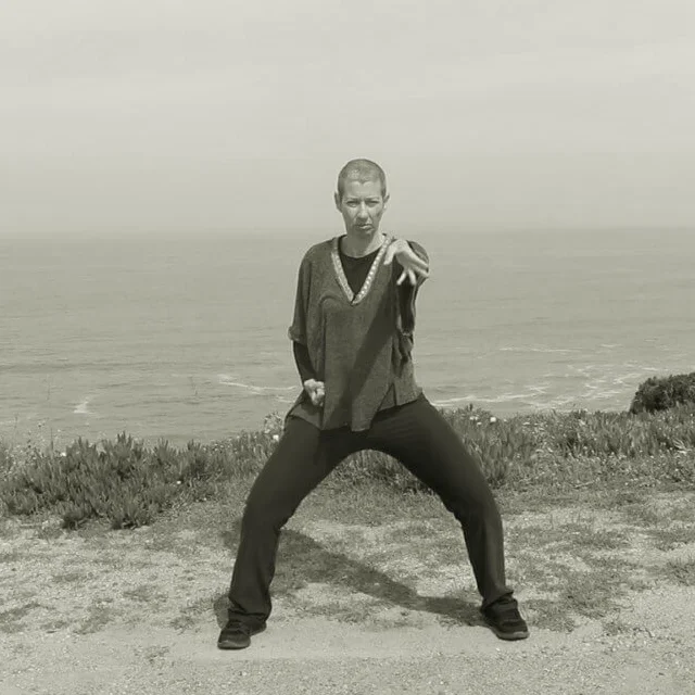 Vanda com as pernas abertas e fletidas, na chamada posição de cavaleiro. Com o punho direito pechado e junto ao corpo e o braço esquerdo estendido.