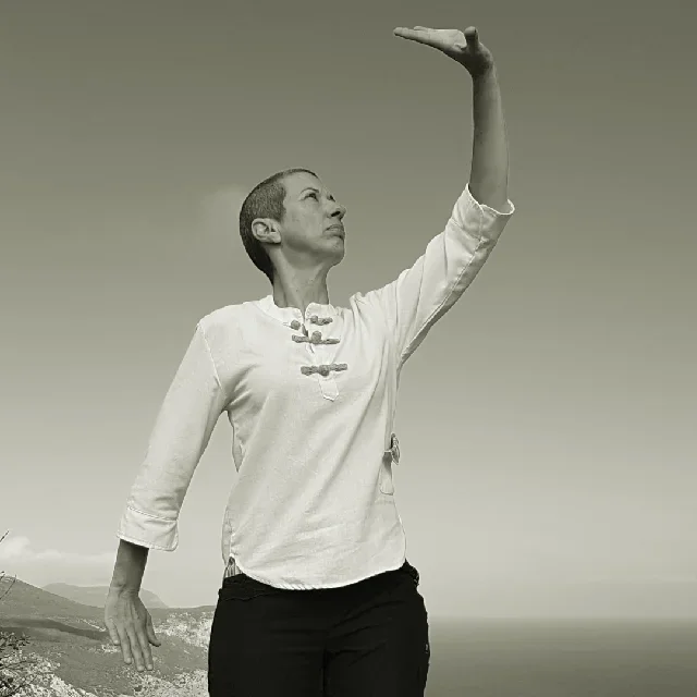 Vanda a praticar um movimento do ba duan jin. O braço esquerdo levantado acima da cabeça com a palma da mão virada para o céu e o braço direito, para baixo, ao lado do corpo, com a palma da mão para a terra.