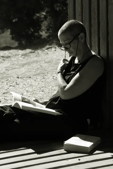 Vanda sentada numa estrutura de madeira, no campo, a ler um livro e outro livro pousado ao lado.