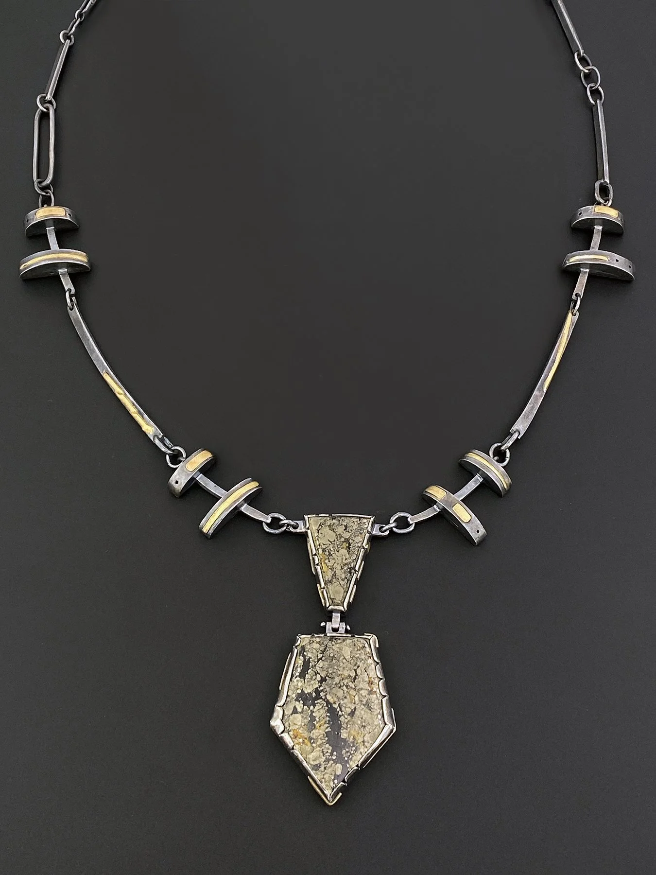 Oxidized silver and 18k gold necklace with geometric links and a hinged chalcopyrite pendant, also known as Apache Gold, in a bold industrial design.