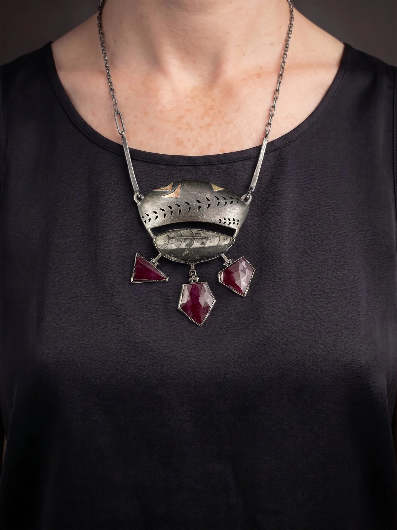 A worn view of the large geometric Orthoceras fossil and ruby statement necklace resting on the chest, showcasing its dramatic 3-inch scale and fluid kinetic movement.
