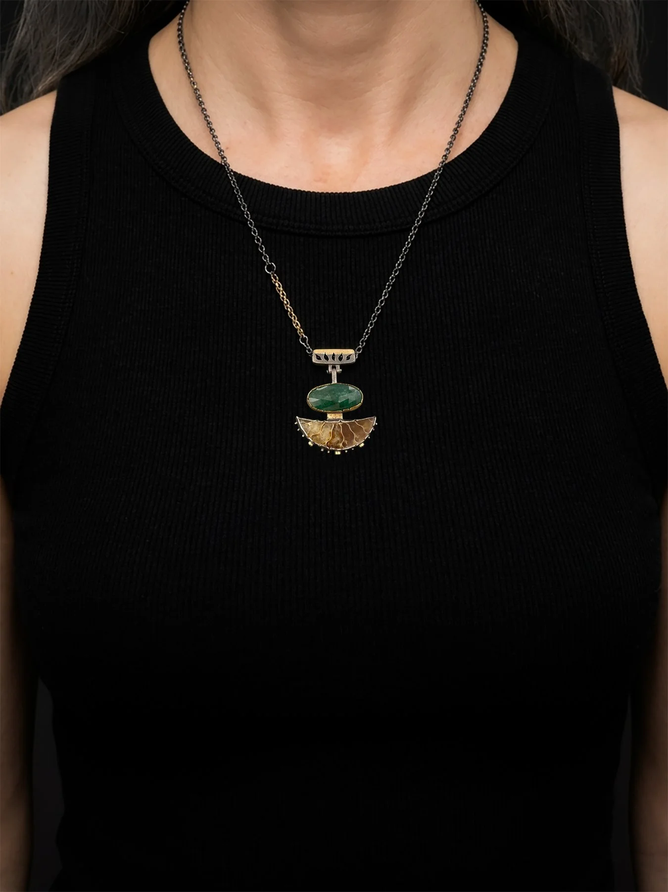 A worn view of the 1.375-inch geometric emerald and ammonite fossil statement necklace resting on the chest, showing the adjustable 16 to 22-inch mixed-metal chain.