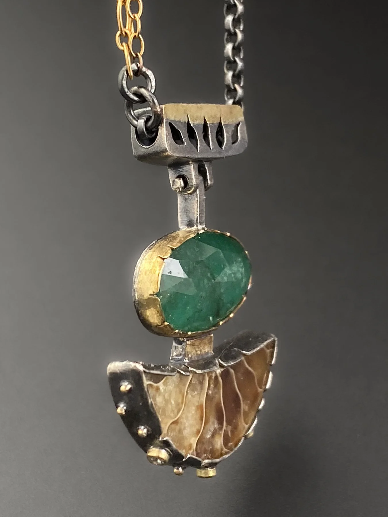 Side view of a vibrant 4.76 carat emerald in a custom handmade 18k yellow gold bezel and ammonite in oxidized silver featuring signature asymmetrical hand-cut notches.