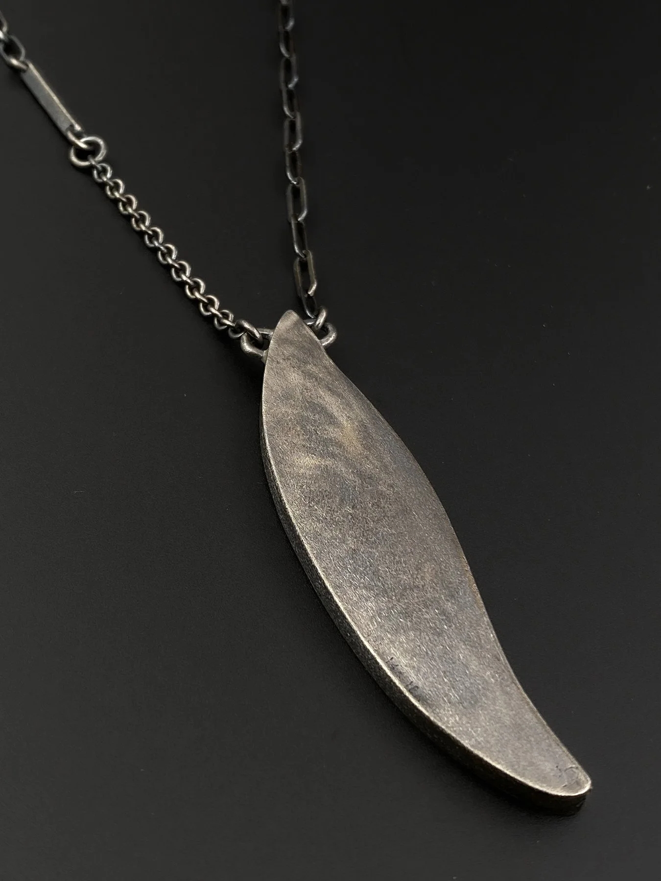 Back profile of the handcrafted feather pendant, showcasing the structural artisan metalwork