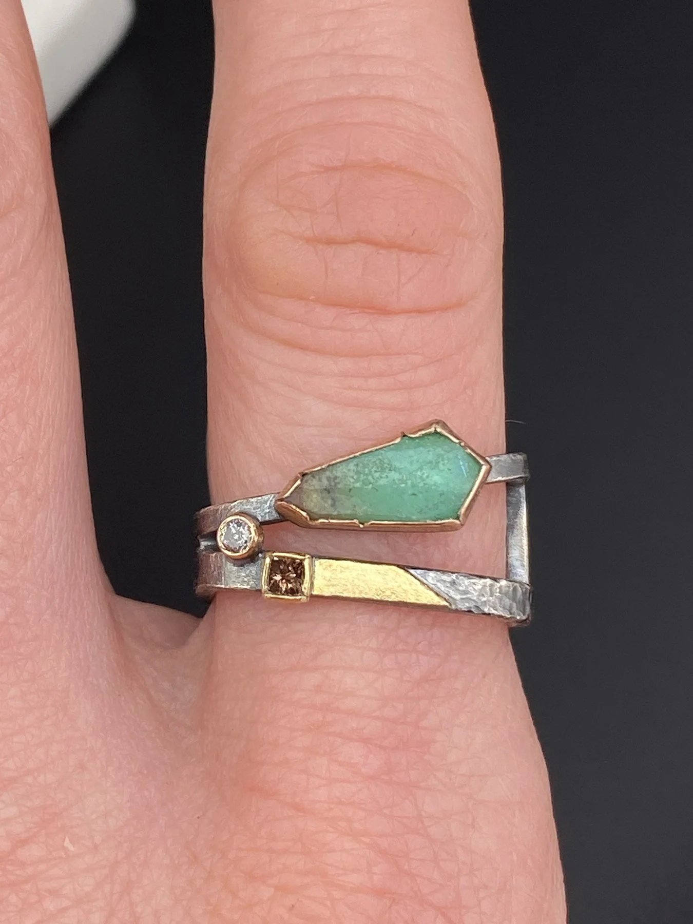 A worn view of an architectural angled square ring featuring a custom-cut green chrysoprase and diamond accents, crafted in oxidized silver, 14k, and 18k gold.