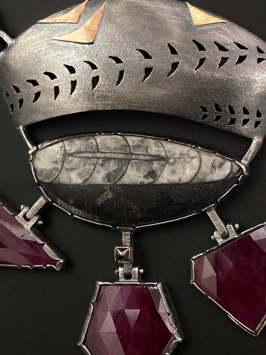 Close-up of a 30-carat Orthoceras fossil set below a pierced oxidized sterling silver hollow form accented with geometric 14k and 18k gold details.
