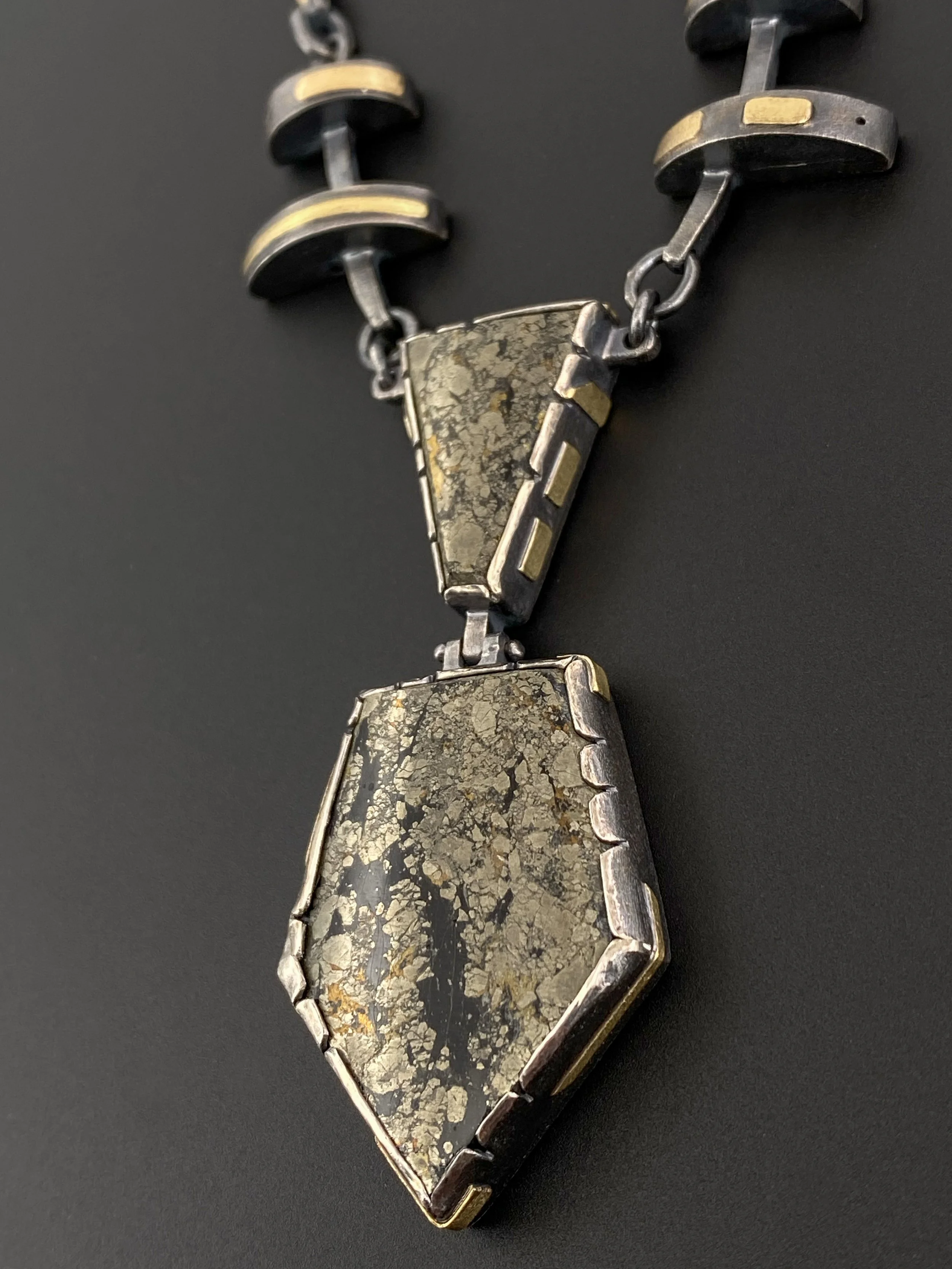 Close up of mixed metal necklace in oxidized sterling silver and 18k gold featuring a cut and hinged chalcopyrite (Apache Gold) pendant with metallic gold and black patterning.