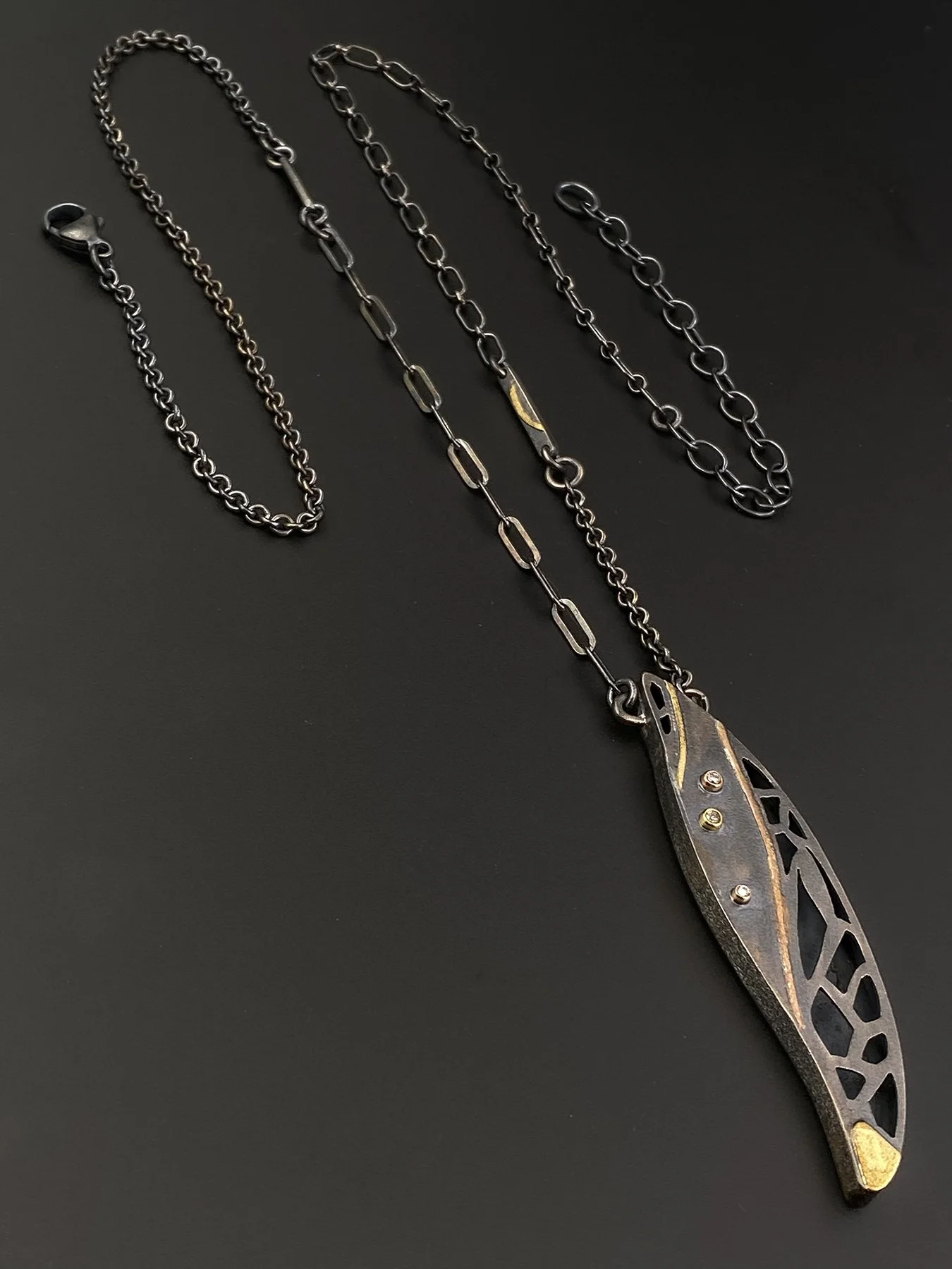 Detail shot of an adjustable mixed-link oxidized sterling silver chain up to 26 inches, featuring a custom asymmetrical metal accent link attached to a feather pendant.