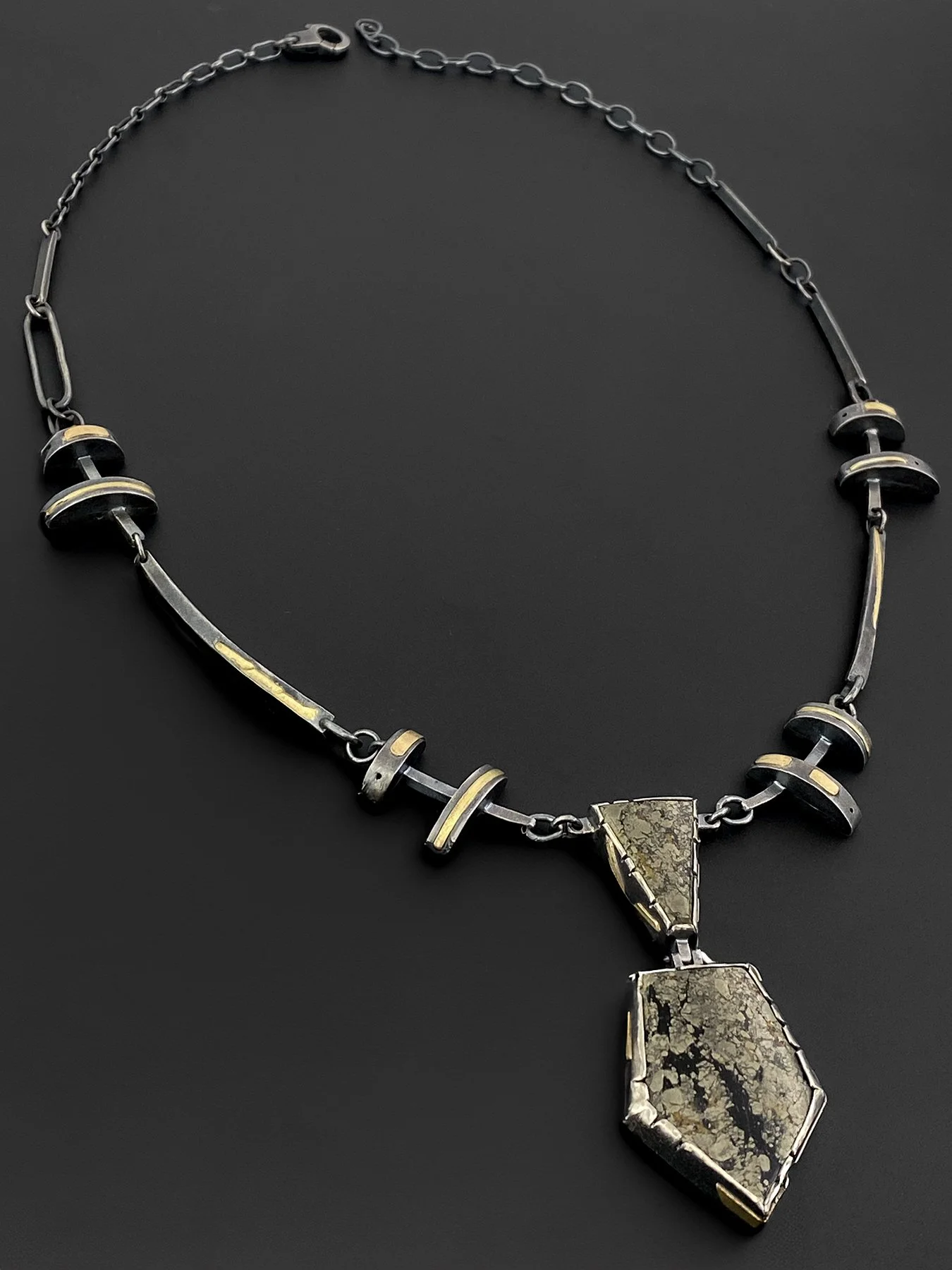 Bold geometric necklace with oxidized silver links and gold accents framing a hinged chalcopyrite pendant with natural metallic gold and dark mineral patterns.