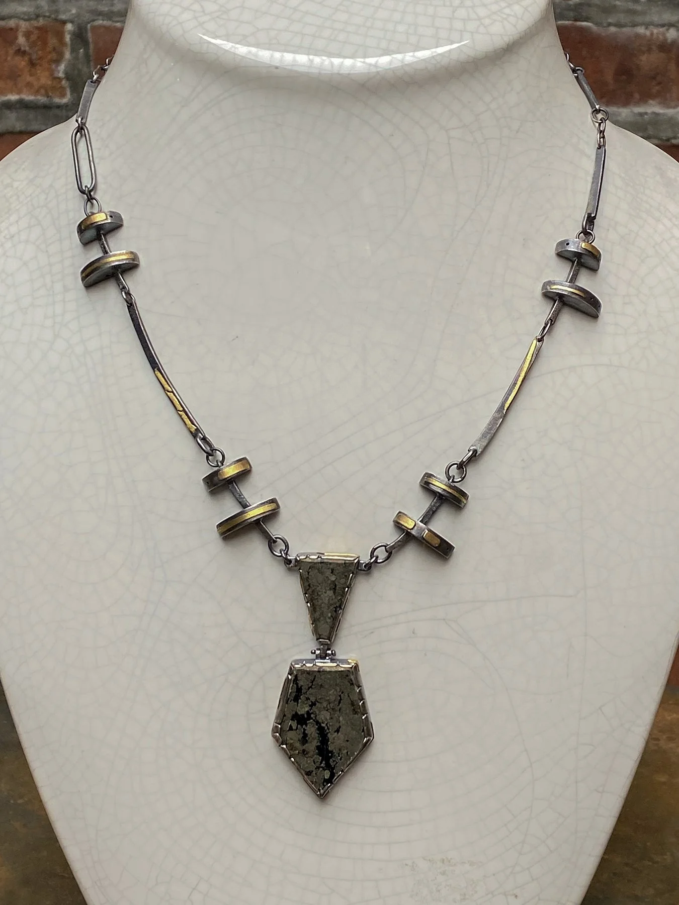 Industrial-style mixed metal necklace displayed on a bust, featuring oxidized silver, 18k gold accents, and a hinged chalcopyrite Apache Gold pendant.