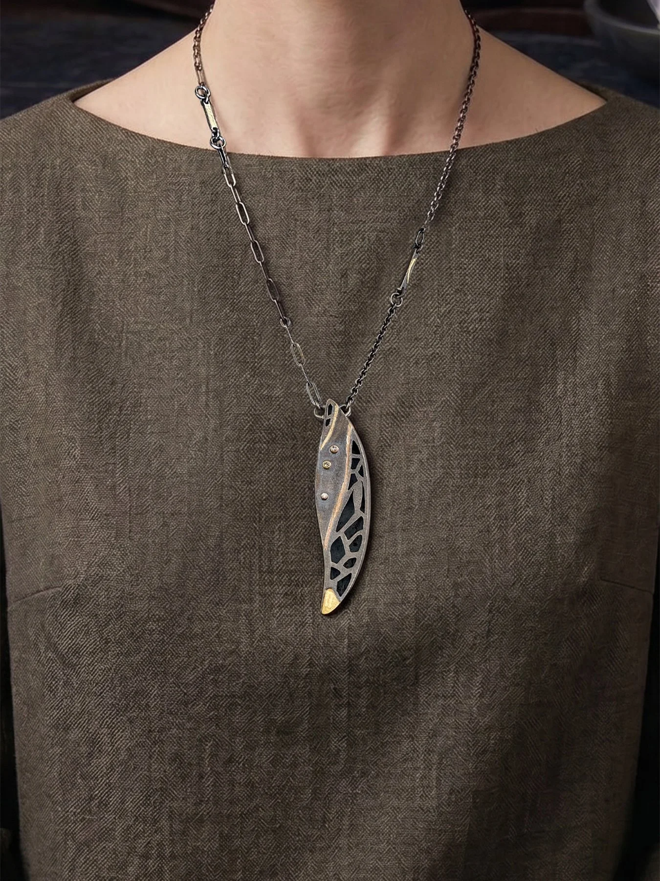 A worn view of the 2.6-inch long mixed-metal feather ajouré diamond pendant resting on the chest, demonstrating its elegant scale and long oxidized silver chain.