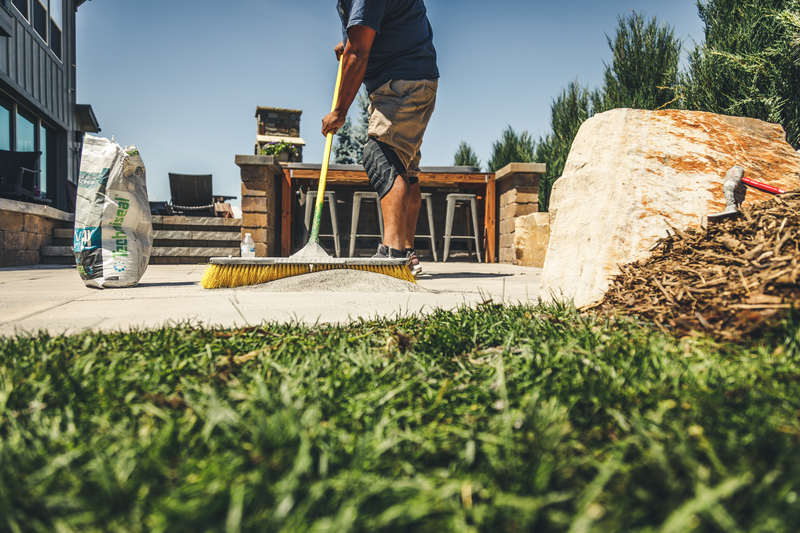 Man sweeping sand in between pavers for an outdoor kitchen for a modern home