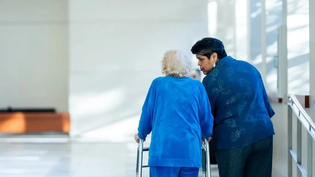 Woman assisting elderly woman down a hallway
