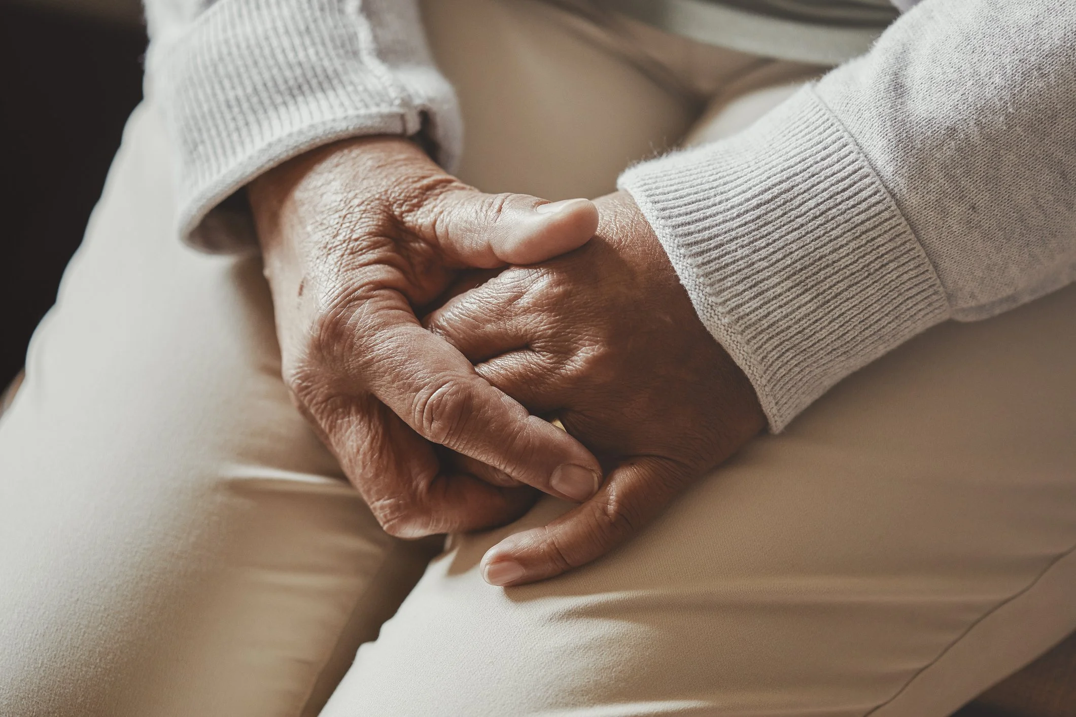 Close-up of two hands clasped, one appears elderly and the other younger, with both wearing long-sleeved clothing.