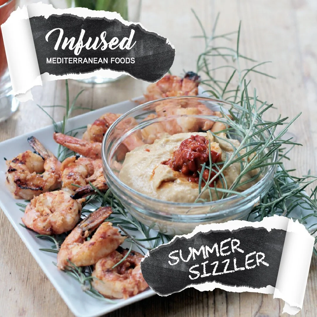 A white square plate with grilled shrimp garnished with green herbs, alongside a small glass bowl of hummus topped with red sauce and herbs, on a wooden surface with a sprig of herbs.