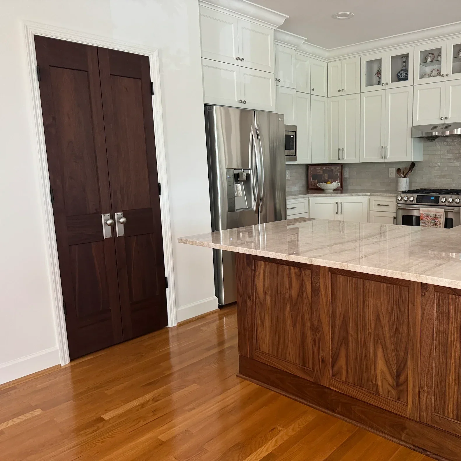 Custom Peruvian walnut double pantry doors in a bright, traditional white kitchen, featuring rich natural wood grain and brushed metal knobs.