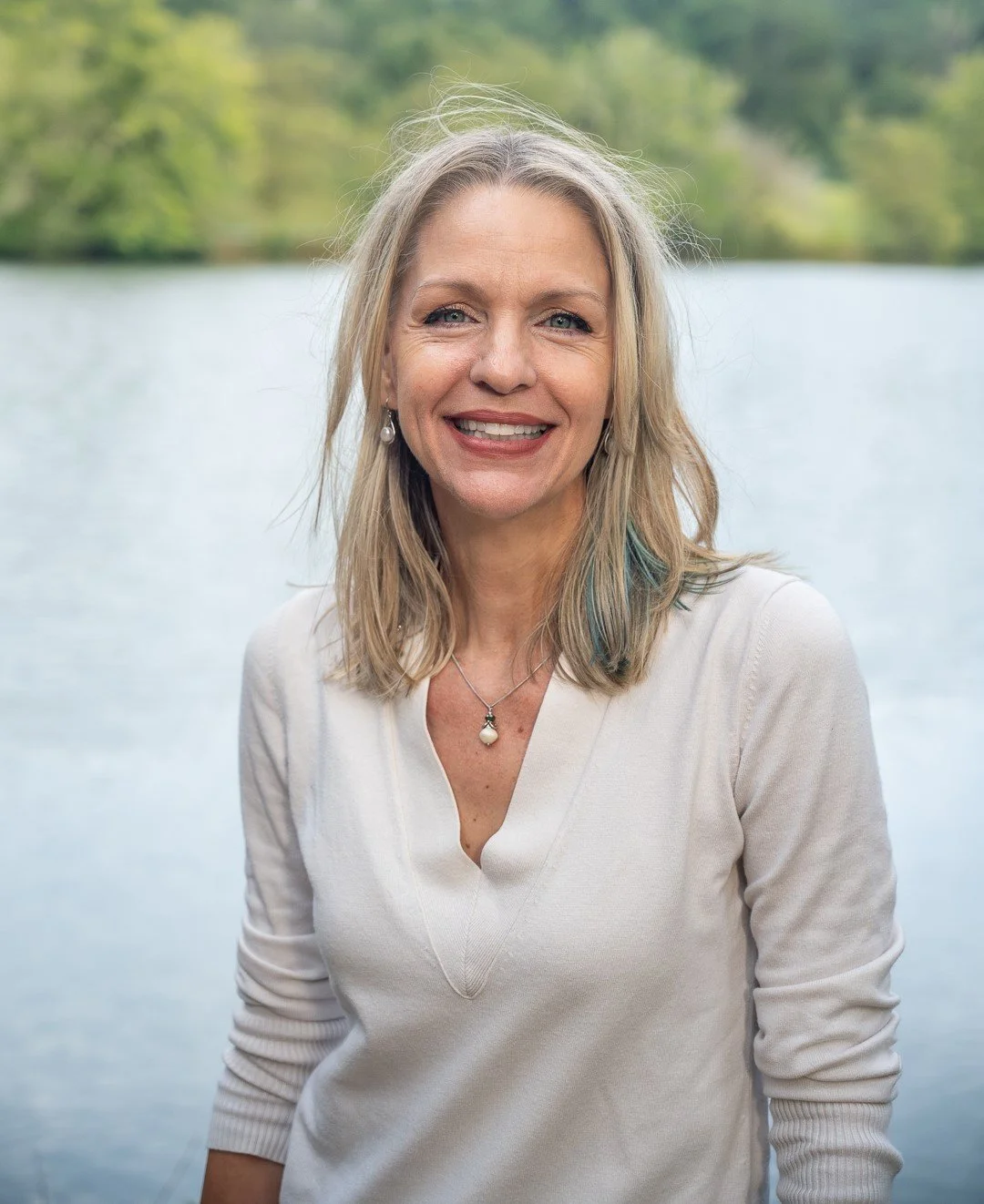 Dr. Robinson wearing a cream sweater standing in front of a lake smiling.