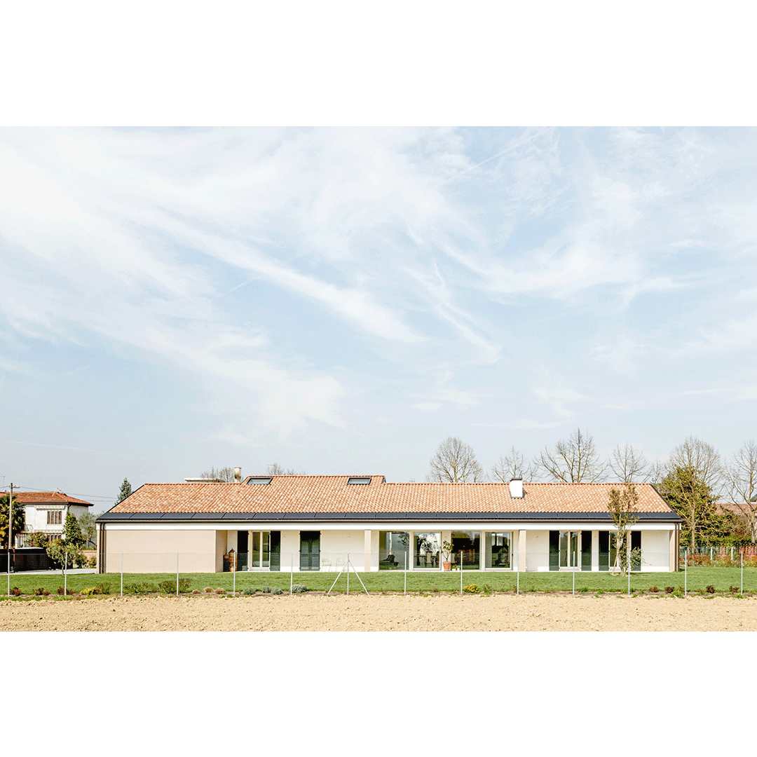 Edificio residenziale con ampio giardino e piante, sotto un cielo sereno con nuvole leggere.