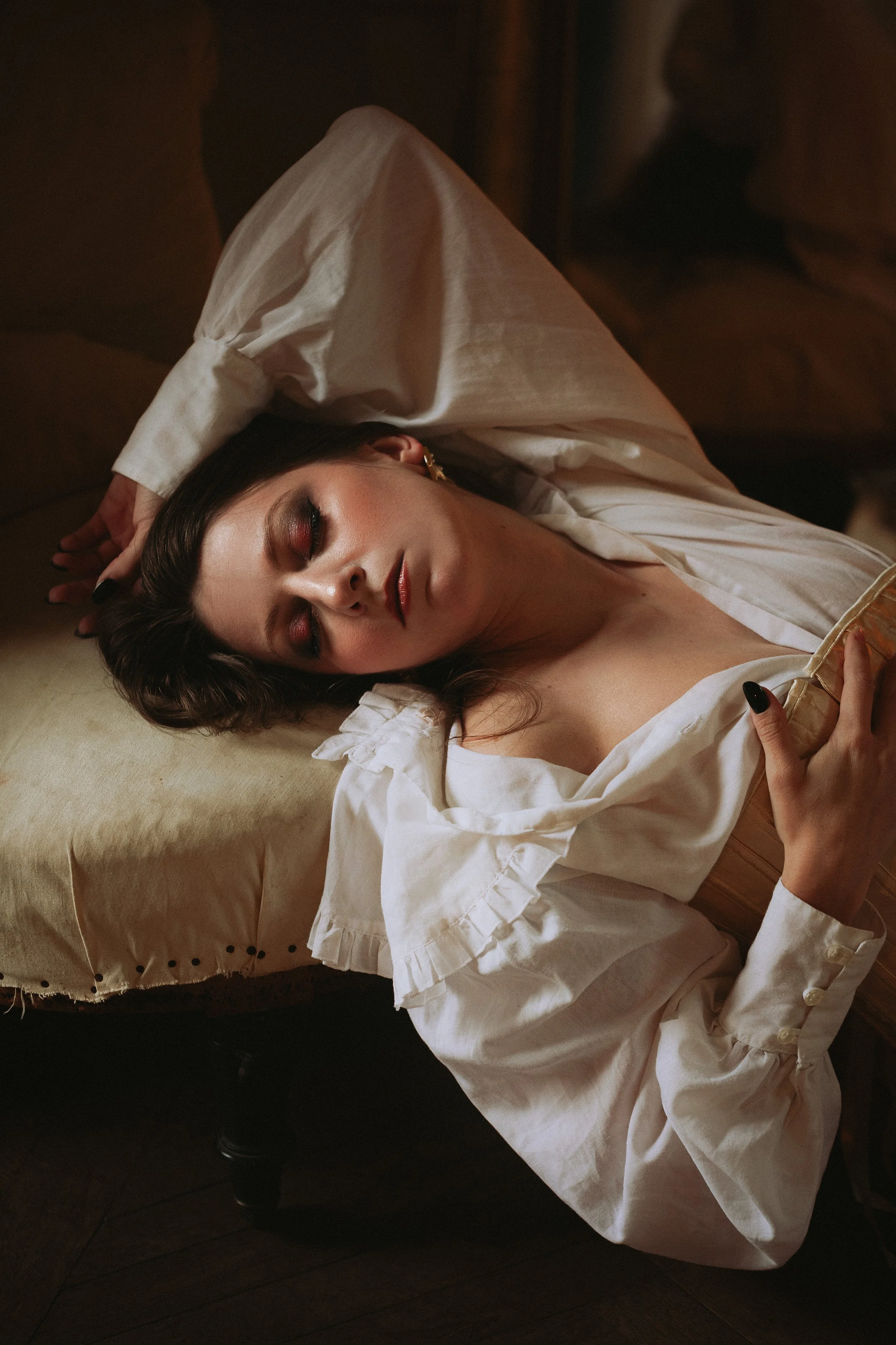 Une femme allongée sur un canapé, portant une blouse blanche avec des détails en volants, avec les yeux fermés et une expression détendue.