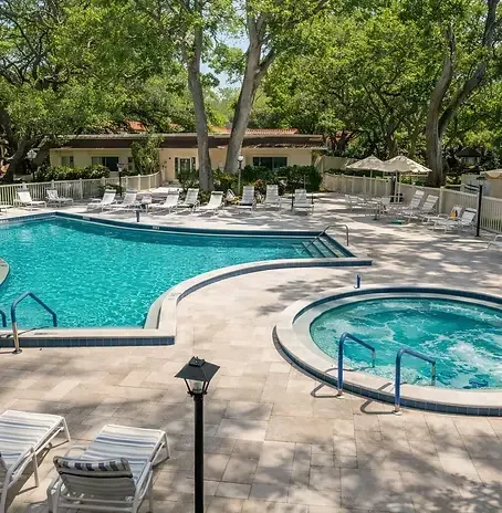 RESORT STYLE CONDO Resort-style pool and hot tub deck at Sunset Getaway in Dunedin, Florida — featuring sun loungers, tropical palm trees, and top-tier amenities, serving as the ultimate relaxation spot after a day riding e-bike trails with Paradise 