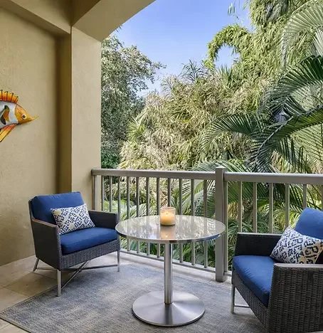 GARDEN Covered patio retreat at Garden Condo in Dunedin, FL — stylish open-air balcony with blue wicker armchairs, tropical greenery views, and close proximity to Honeymoon Island beaches and local e-bike trails.