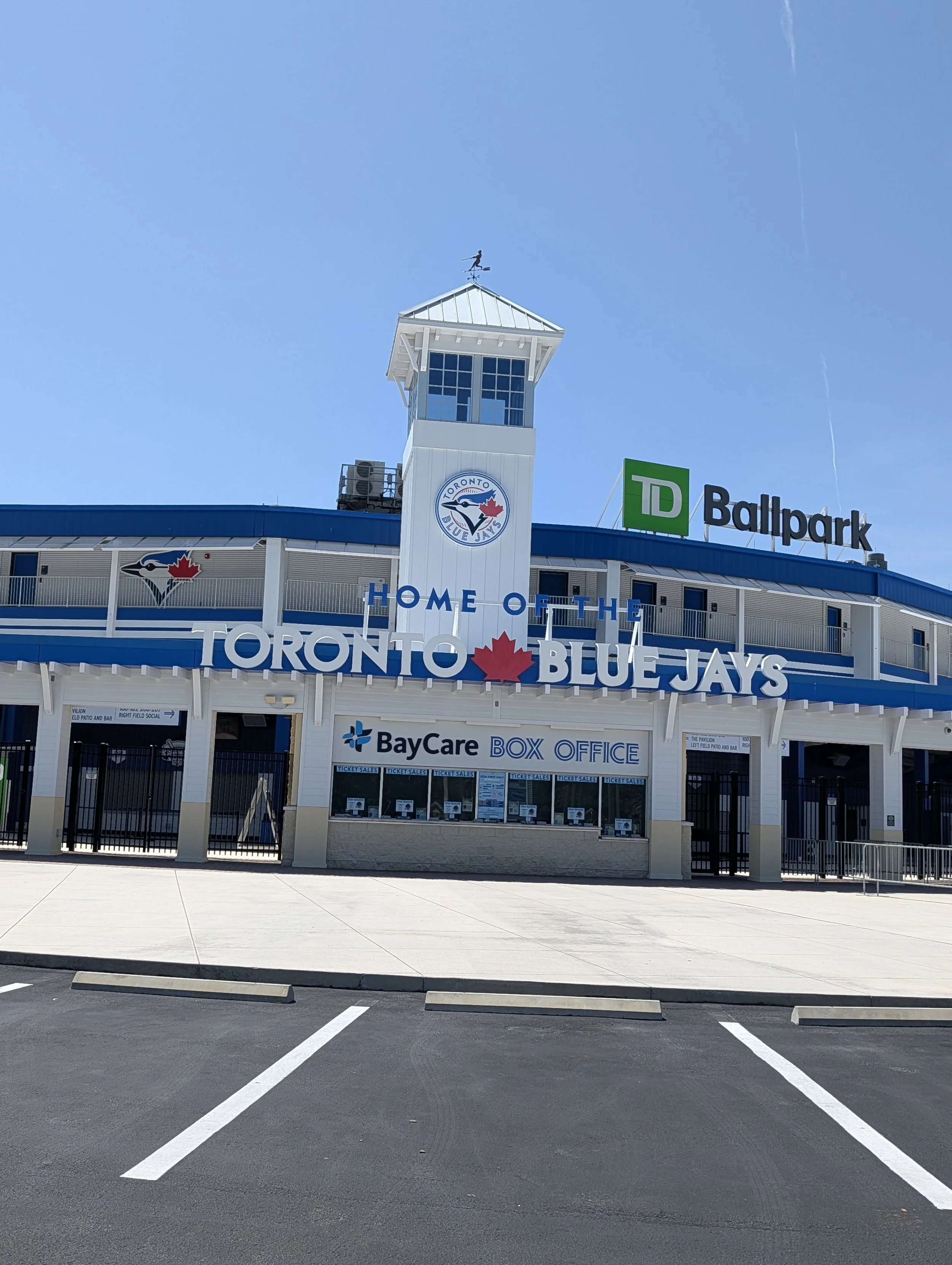 Exterior view of the Rogers Centre stadium with Toronto Blue Jays signage, a clock tower, and a mostly empty parking lot.