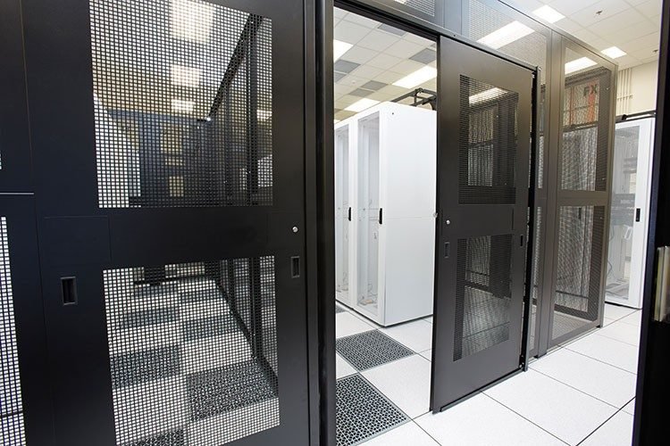 Server racks and data center cabinets with black mesh doors in a server room behind a data center cage.