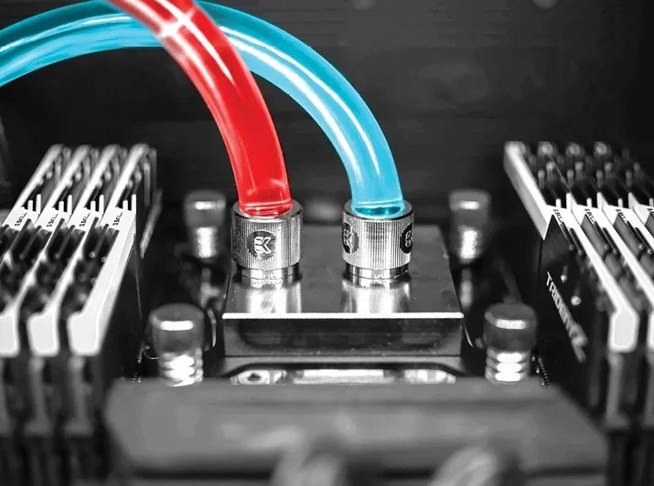 Close-up of a computer water cooling setup with red and blue transparent tubes connected to a metal block on a motherboard.