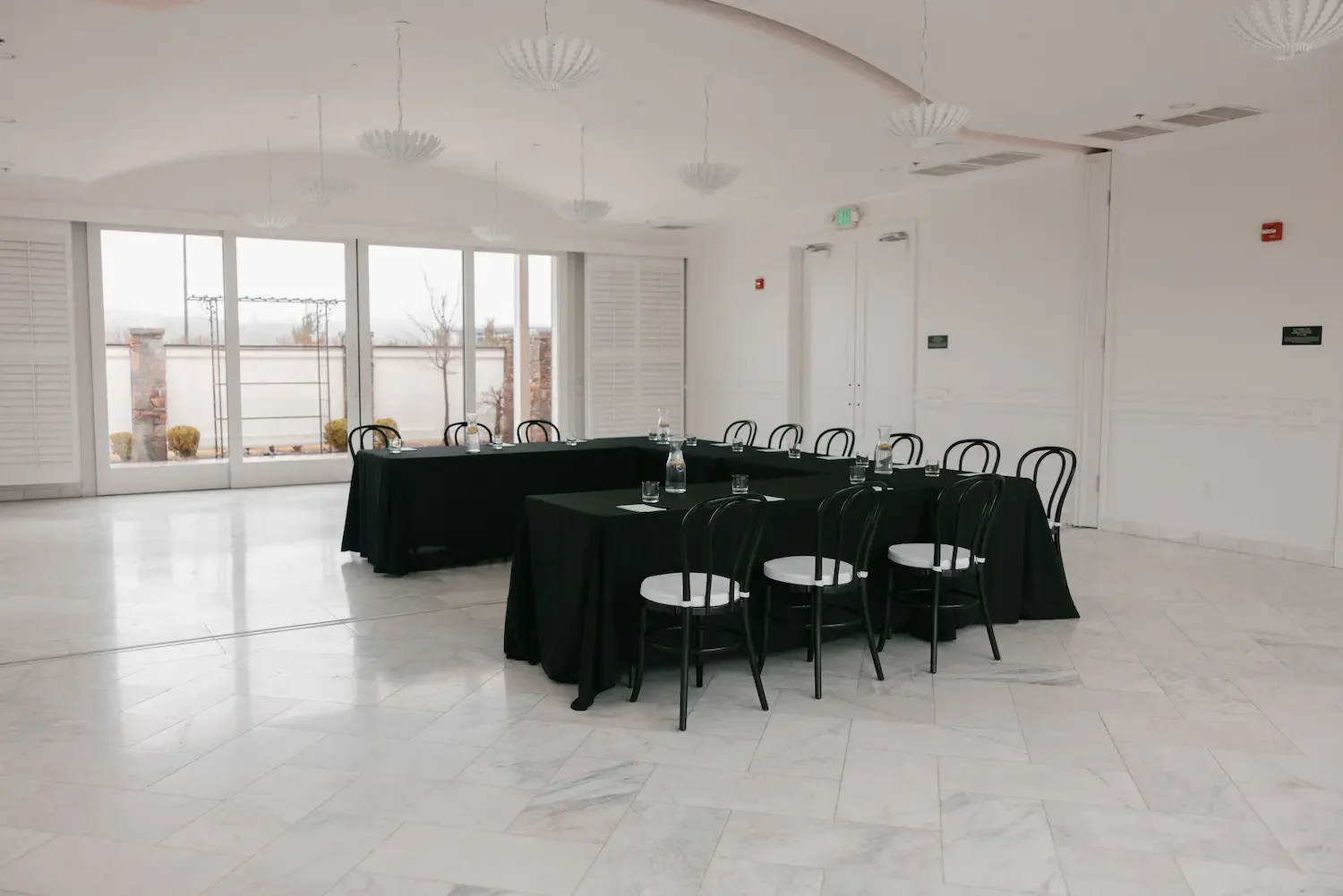 Empty conference room with black tables, white chairs, glass water bottles, and a large window with outside view