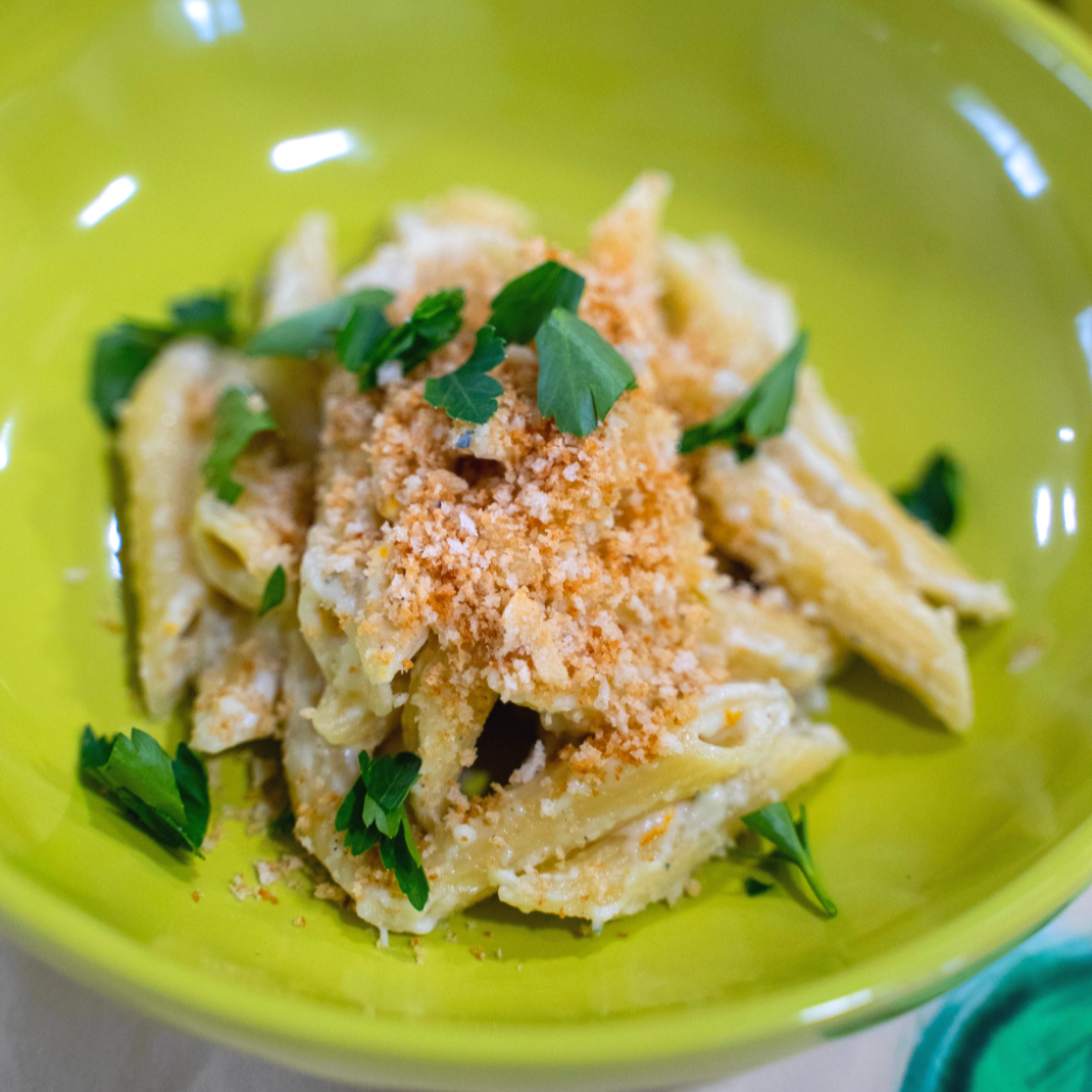 A bowl of mac and cheese penne pasta, topped with breadcrumbs and parsley