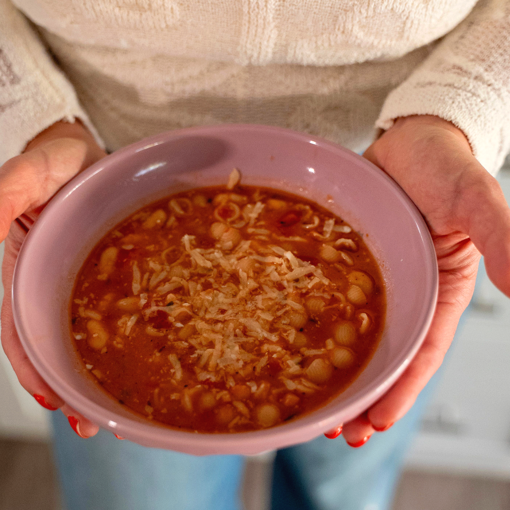 Close-up of pasta e fagioli with beans and pasta in a tomato-based broth served in a purple bowl