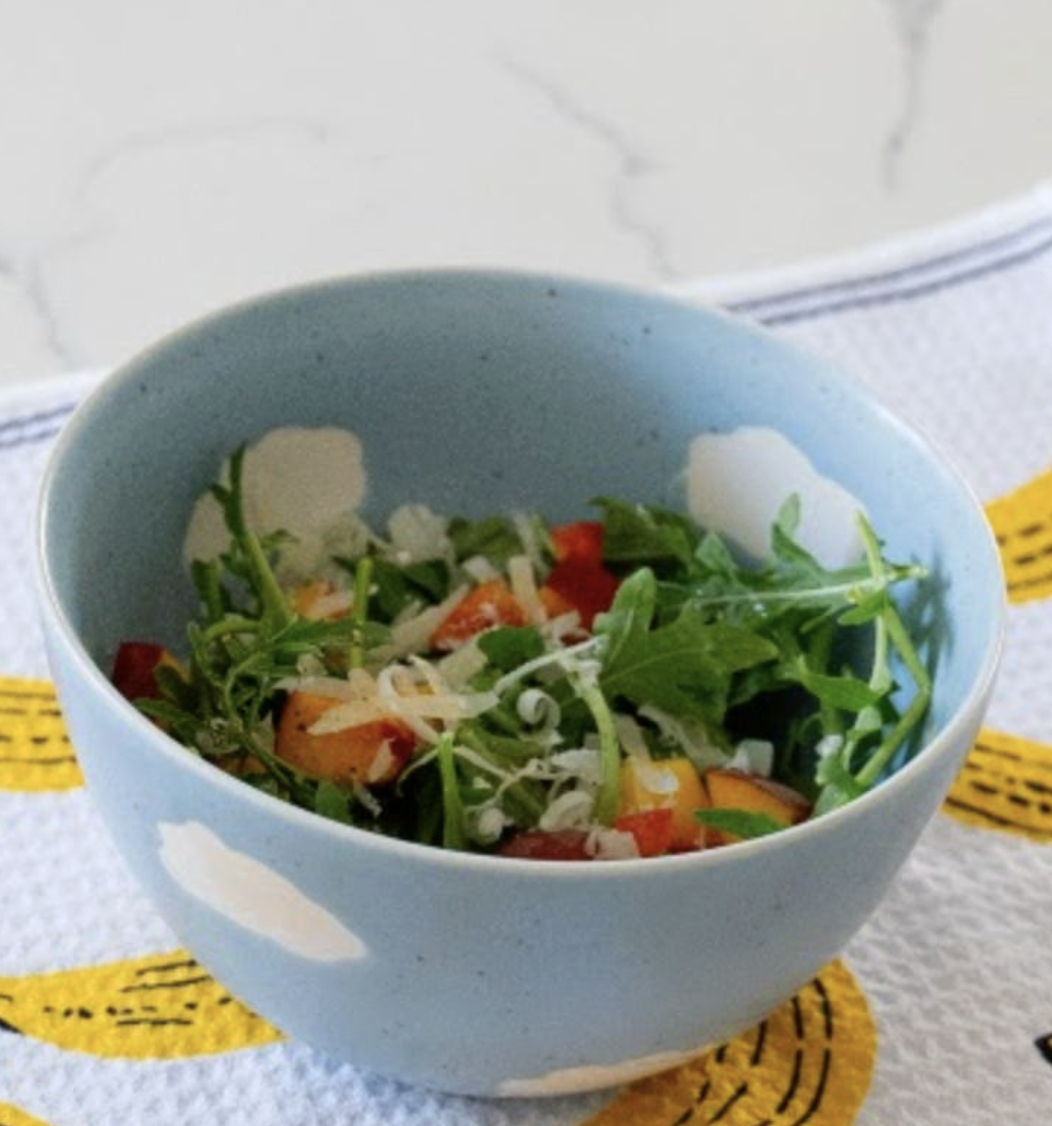 An arugula, peach, and Parmesan salad in a blue bowl