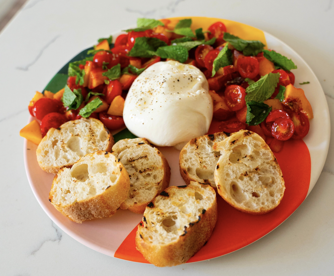 A plate of mint, peach and cherry tomato salasa served with burrata and grilled baguette slices