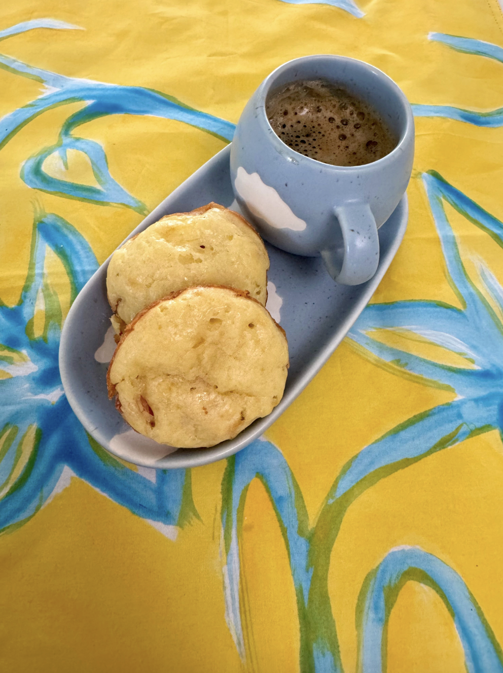 A close up of two tapioca breakfast muffins and espresso cup sits on a yellow and blue patterned tablecloth