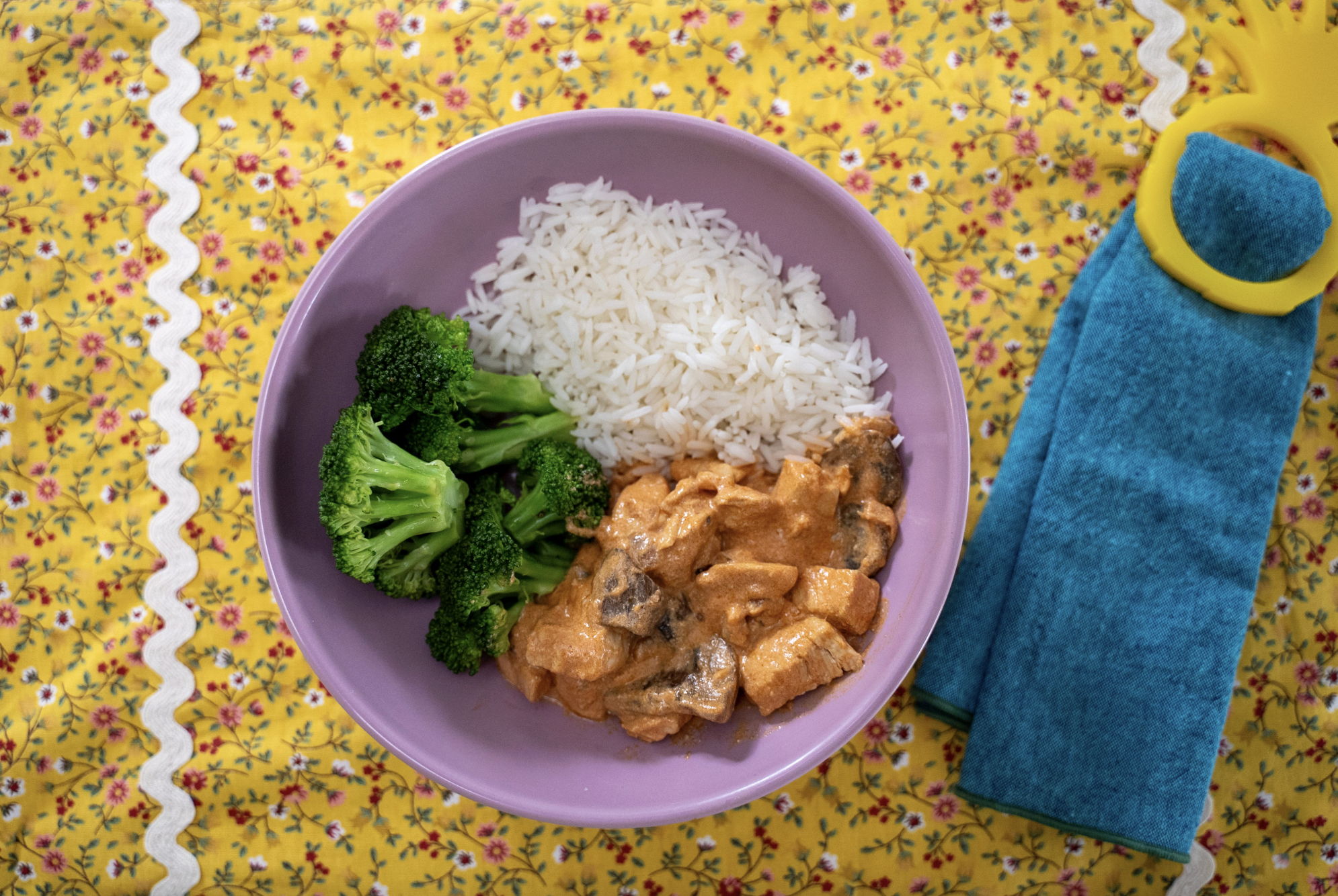 Close-up of brazilian chicken estrogonofe made with mushrooms and a lighter tomato yogurt sauce, served with white rice and broccoli in a purple bowl.
