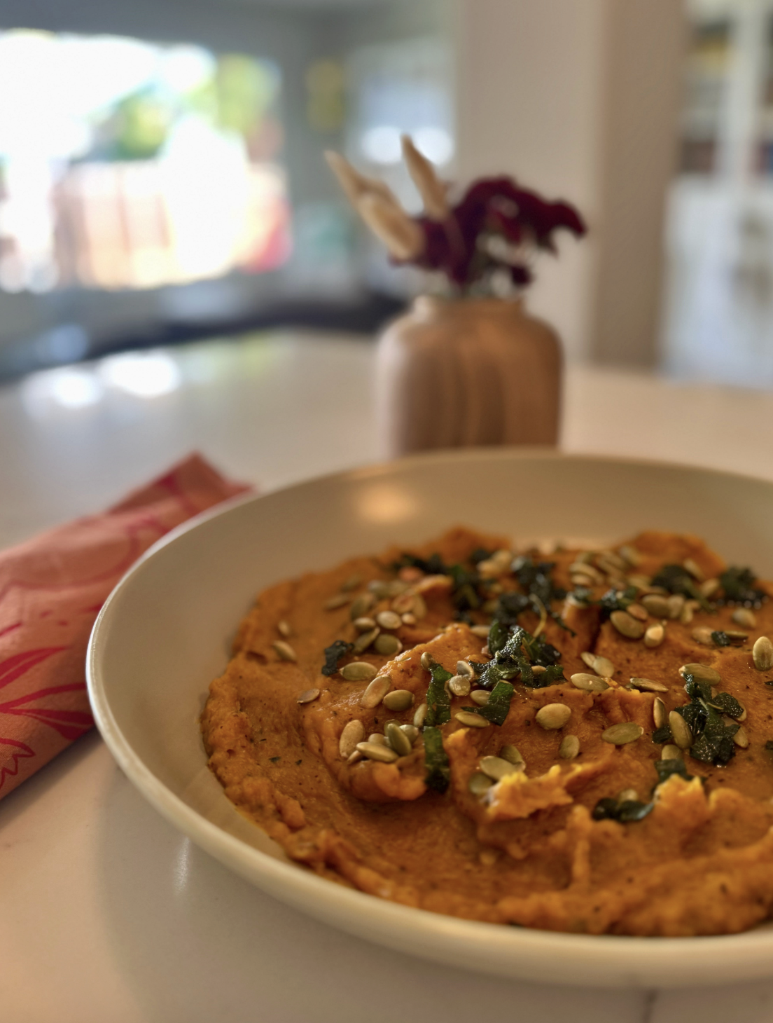 A close up of a bowl of quibebe, roasted butternut squash mash topped with pumpkin seeds and sage leaves