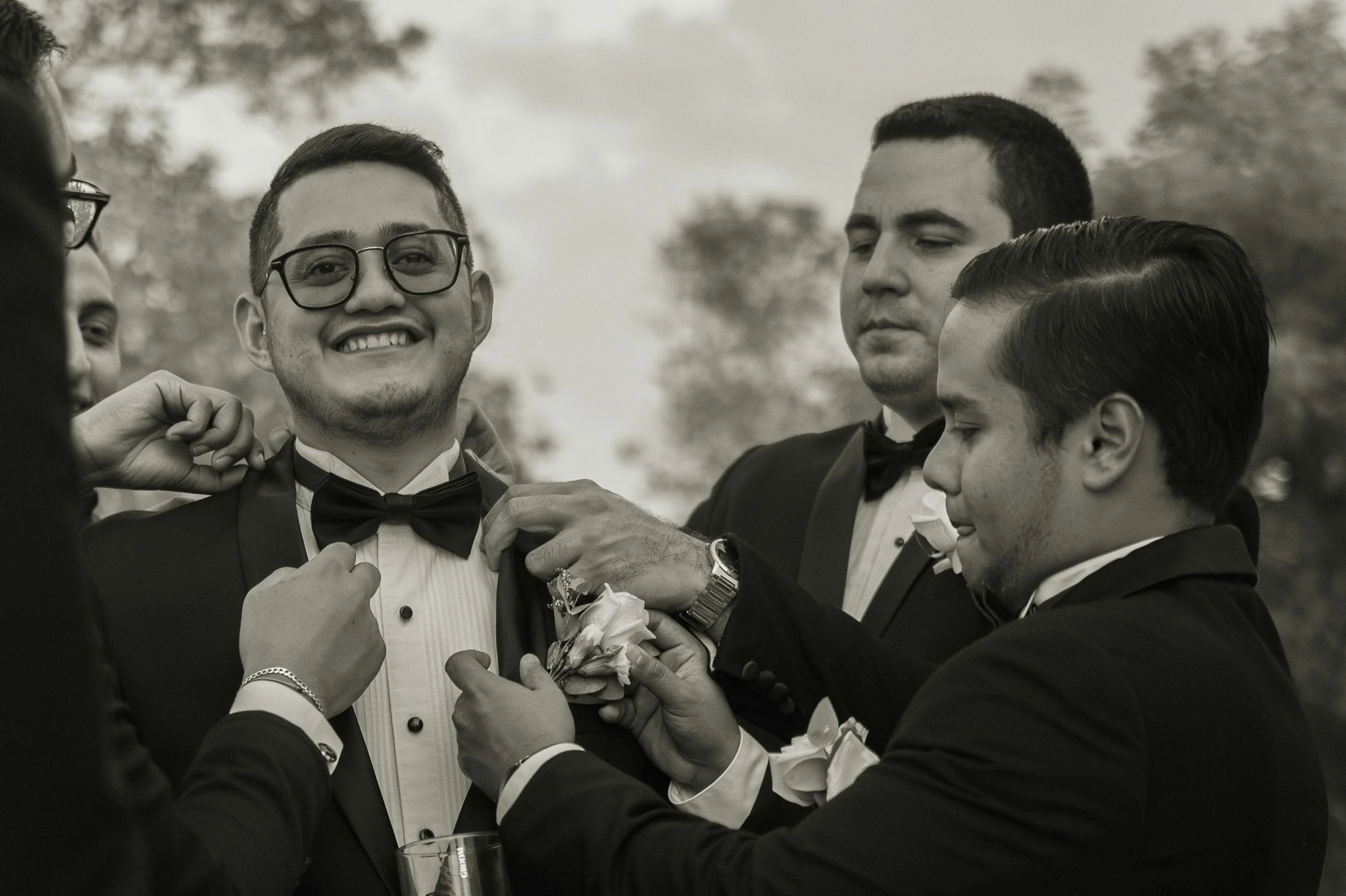 Group of men in tuxedos, one smiling, some adjusting boutonnières.