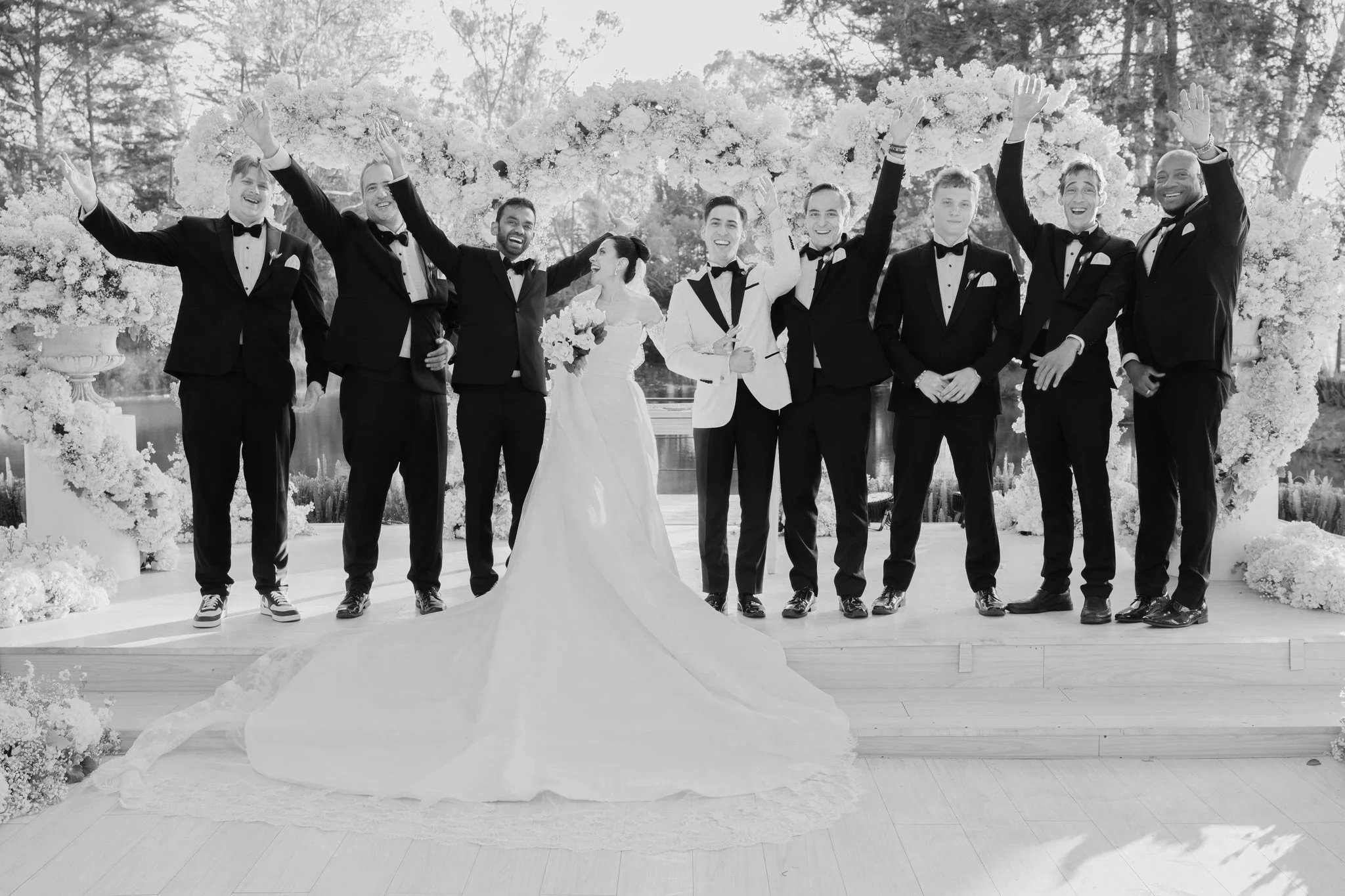 Group of men in tuxedos, one smiling, some adjusting boutonnières.