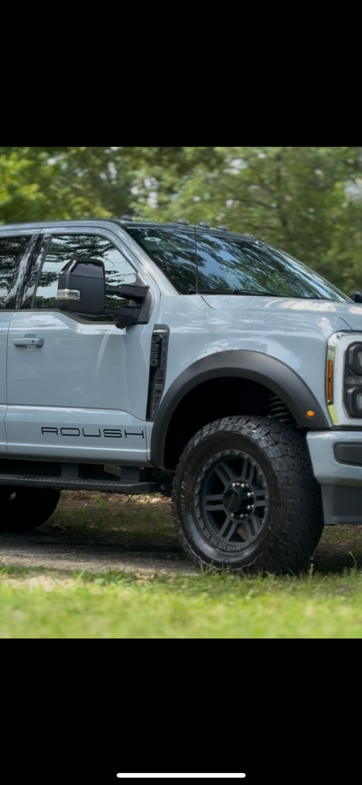 A blue sports car parked on a dirt surface with trees and power lines in the background during dusk.