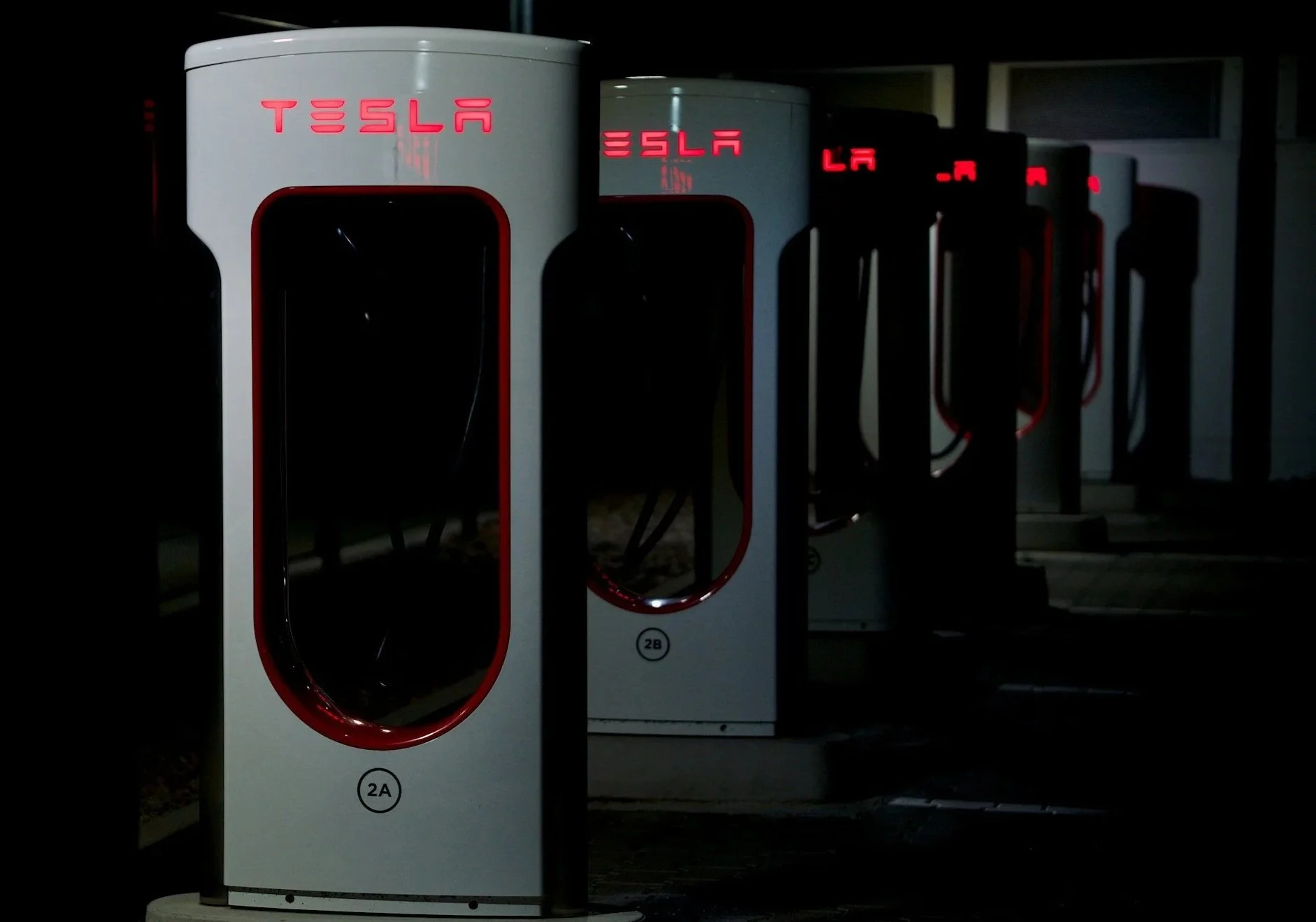 Electric vehicle charging stations with illuminated 'TESLA' signs at night.