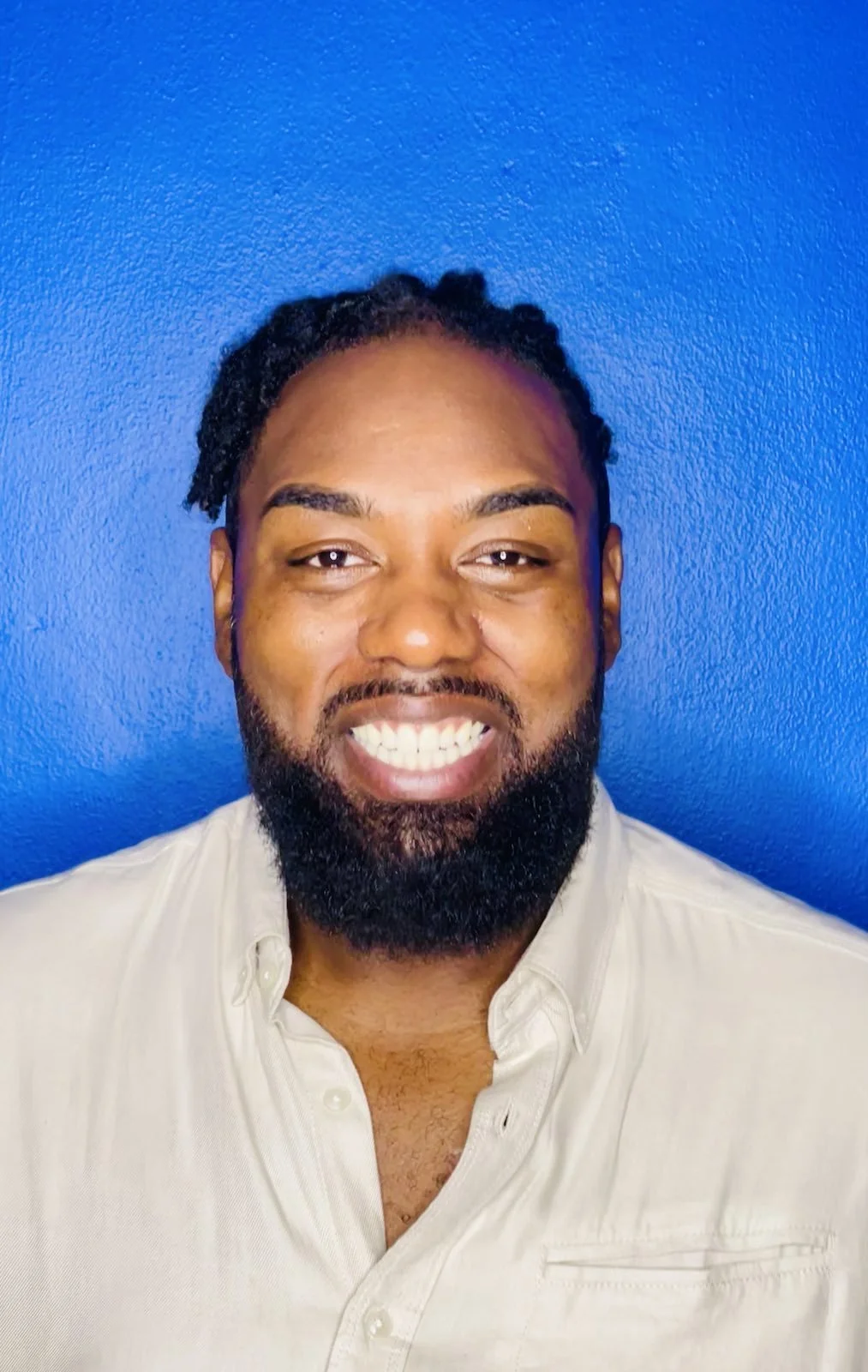 A man with a beard smiling in front of a blue wall.
